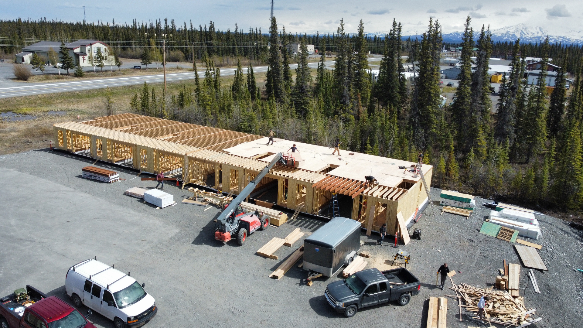 Aerial view of a long commercial building with wall framing and roof deck going on, crew and telehandler on site