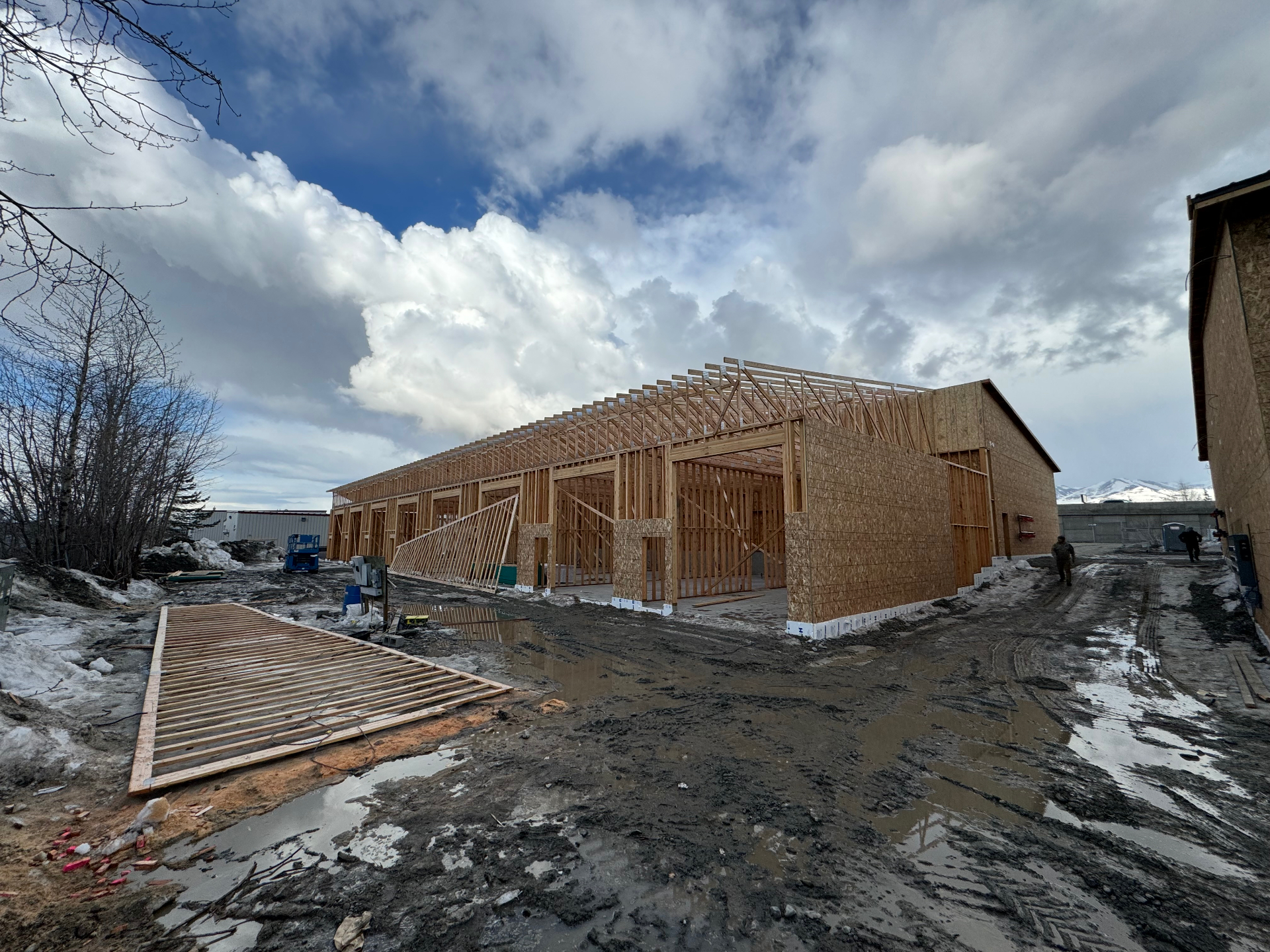 Large commercial building shell framed with trusses set, snow and mountains beyond