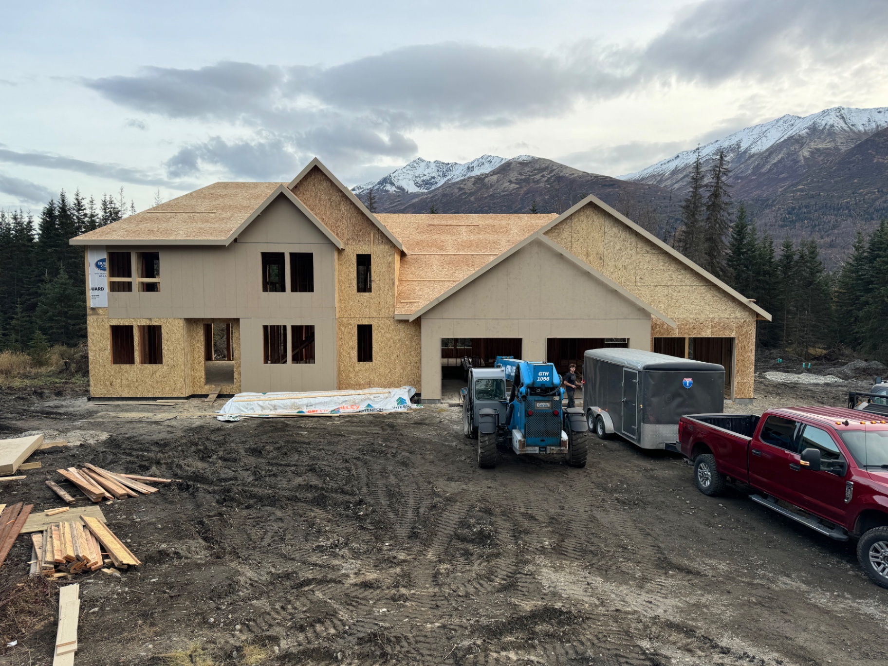 Large sheathed two-story home with three-car garage framed below snowy mountains
