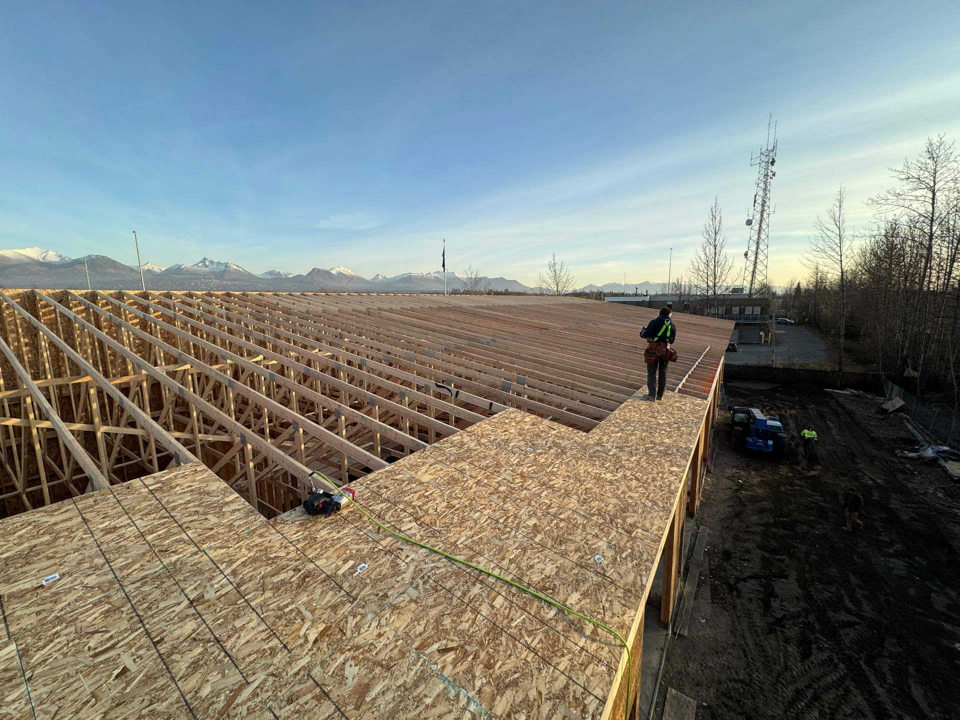 Large commercial roof truss system being sheathed with mountains in the background