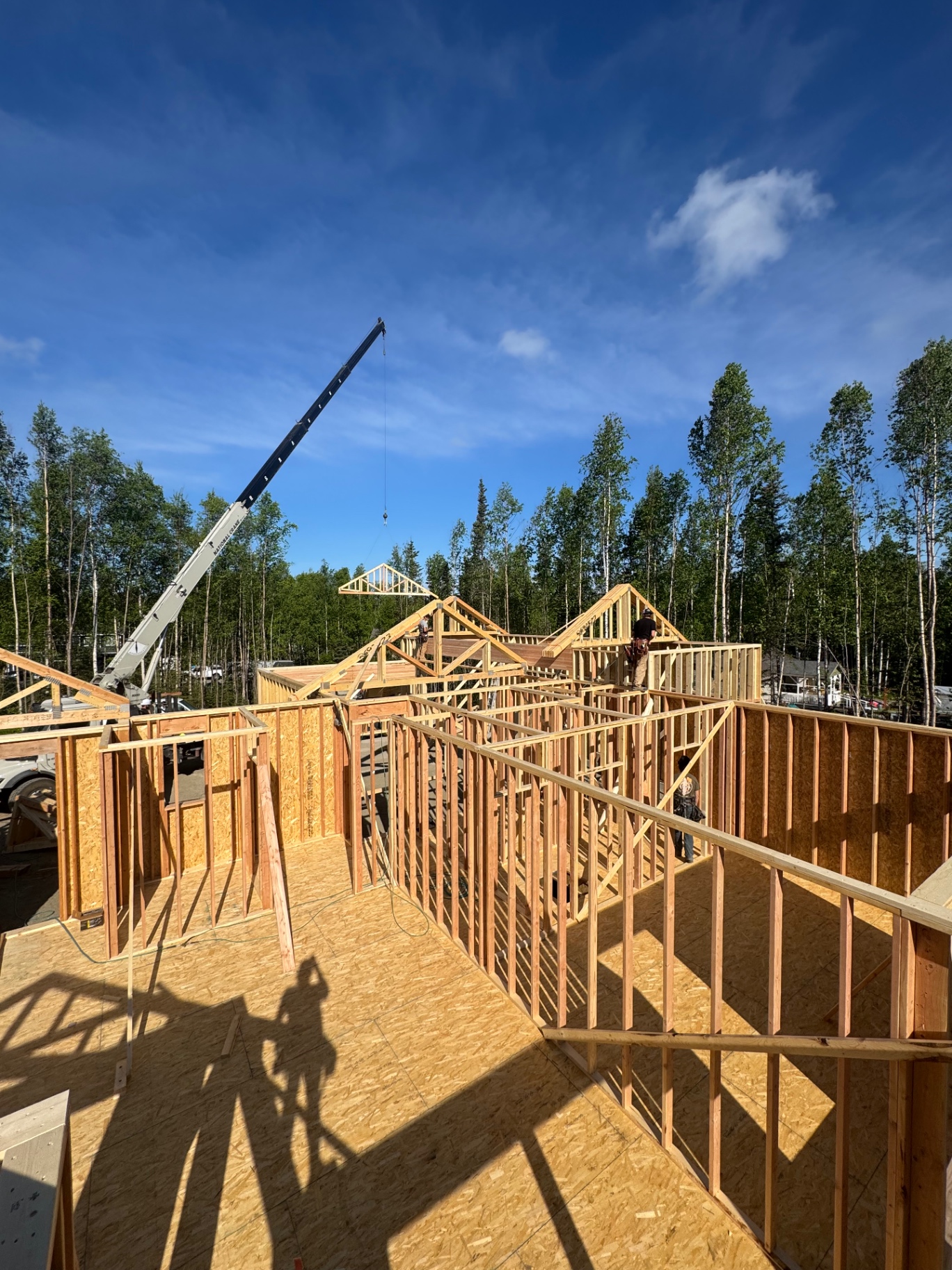 Crane setting roof trusses on a newly framed single-family home under blue sky